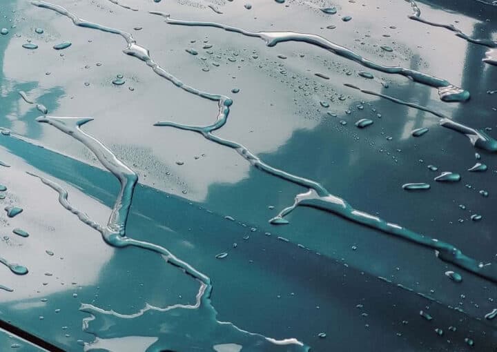 Water droplets on a glossy car hood reflecting the sky
