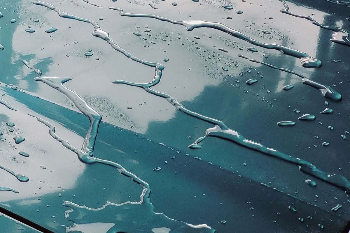 Water droplets on a glossy car hood reflecting the sky