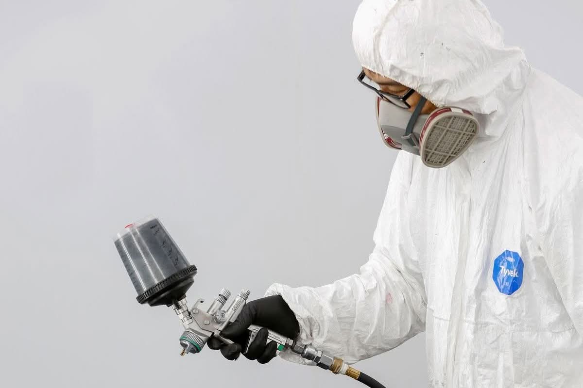 Technician in protective gear spray painting a car bumper