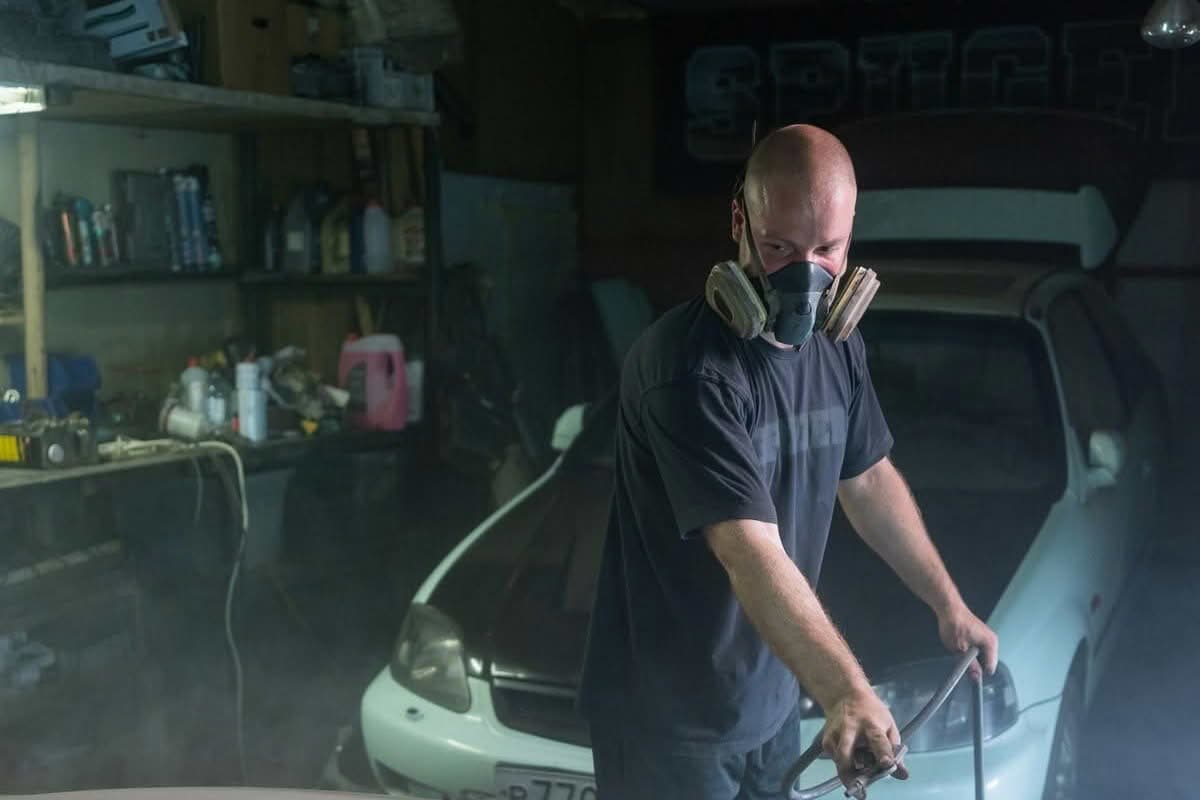 Technician spray painting a car panel in a workshop