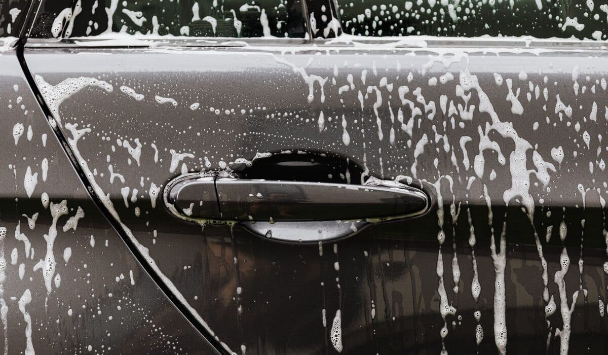 Soap suds rinsing down a car door panel during a hand wash to protect the paint finish