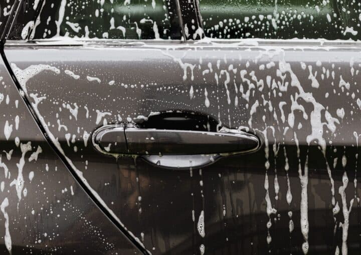 Soap suds rinsing down a car door panel during a hand wash to protect the paint finish