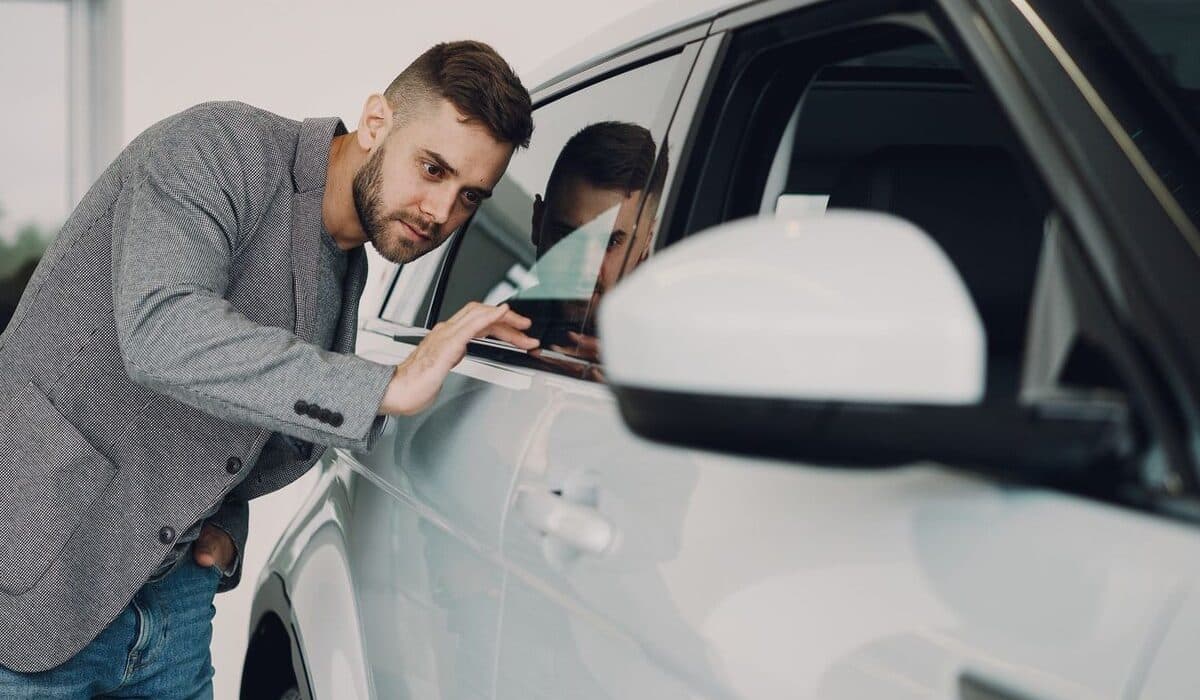 Prospective buyer closely inspecting a cars paint and body panel before purchase