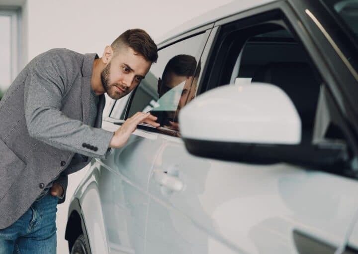 Prospective buyer closely inspecting a cars paint and body panel before purchase
