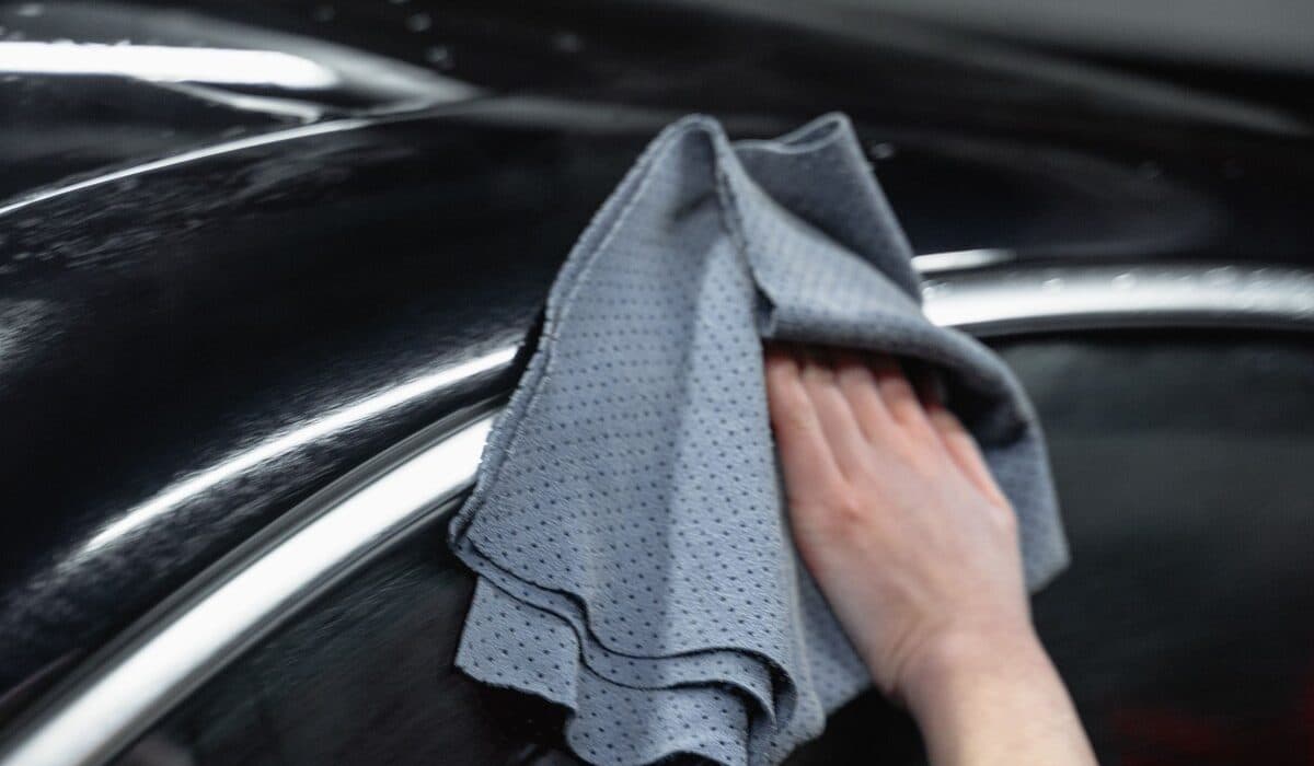 Hand carefully hand-wiping a finished car panel with a microfiber cloth after paint restoration work