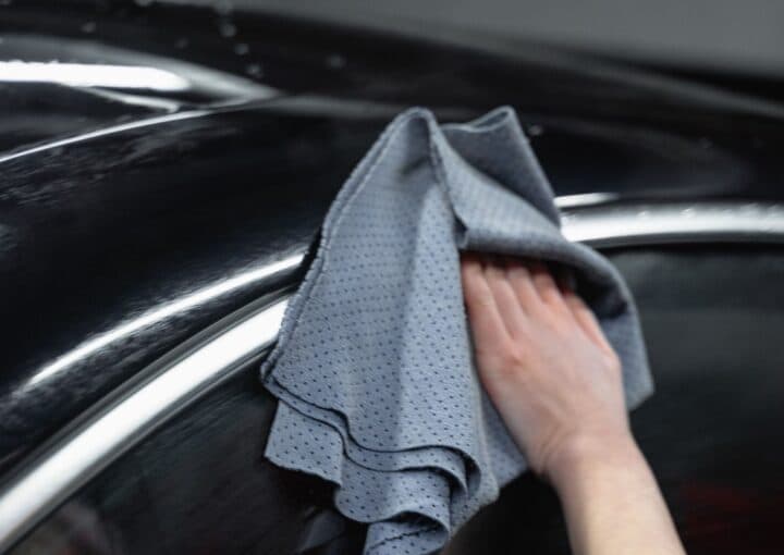 Hand carefully hand-wiping a finished car panel with a microfiber cloth after paint restoration work