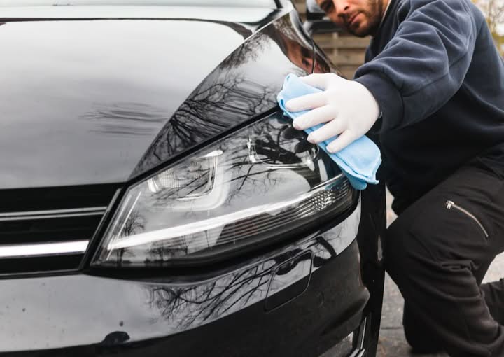 Person wiping down a car headlight with a cloth