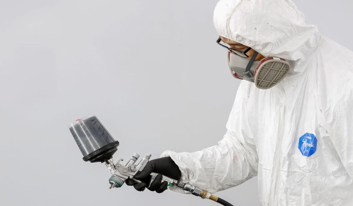 Technician in protective gear spray painting a car bumper