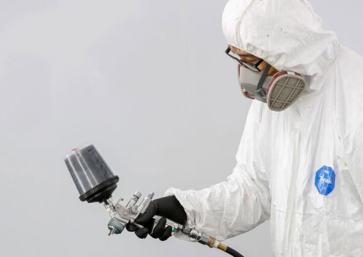Technician in protective gear spray painting a car bumper