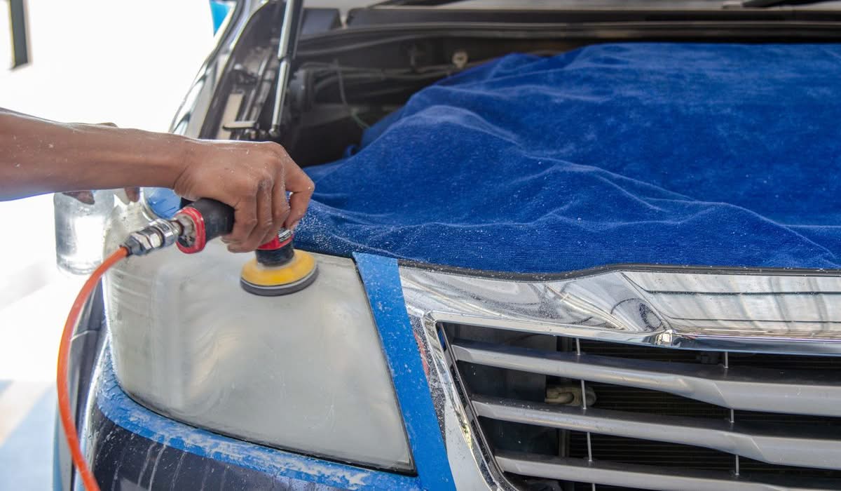 Technician polishing a foggy car headlight during restoration