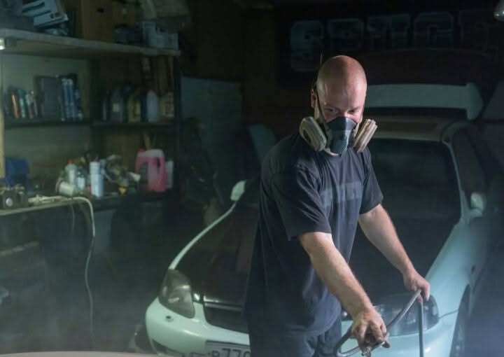 Technician spray painting a car panel in a workshop