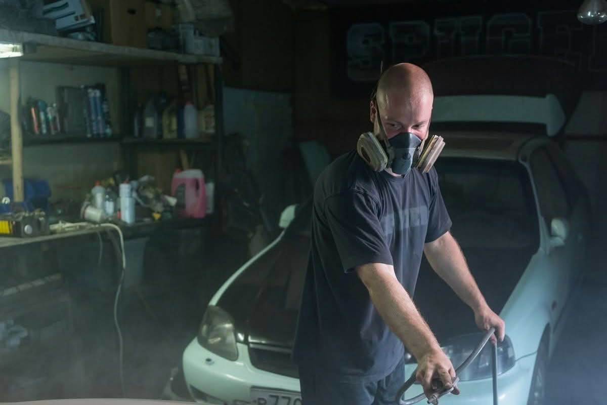Technician spray painting a car panel in a workshop