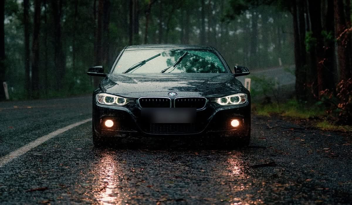 Car driving through a rainy forest road at dusk with headlights on