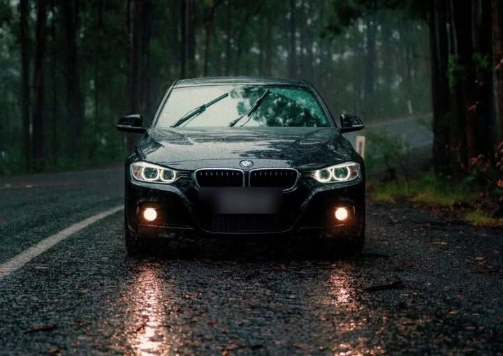 Car driving through a rainy forest road at dusk with headlights on