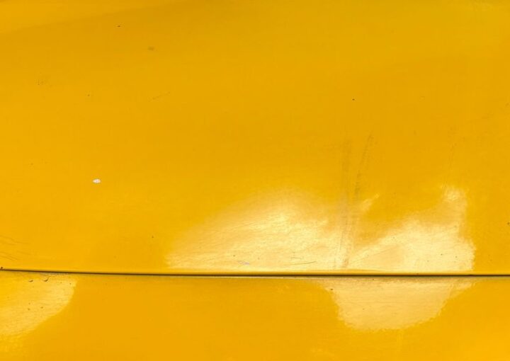 Close-up of light surface scratches and swirl marks on a cars glossy yellow paint